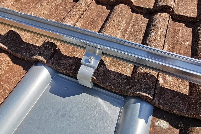Aluminiumschiene mit Halteklemme über einem Blechziegel auf dem Ziegeldach