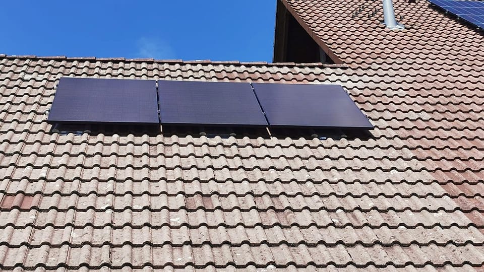 Drei schwarze Photovoltaikmodule auf einem roten Ziegeldach vor blauem Himmel