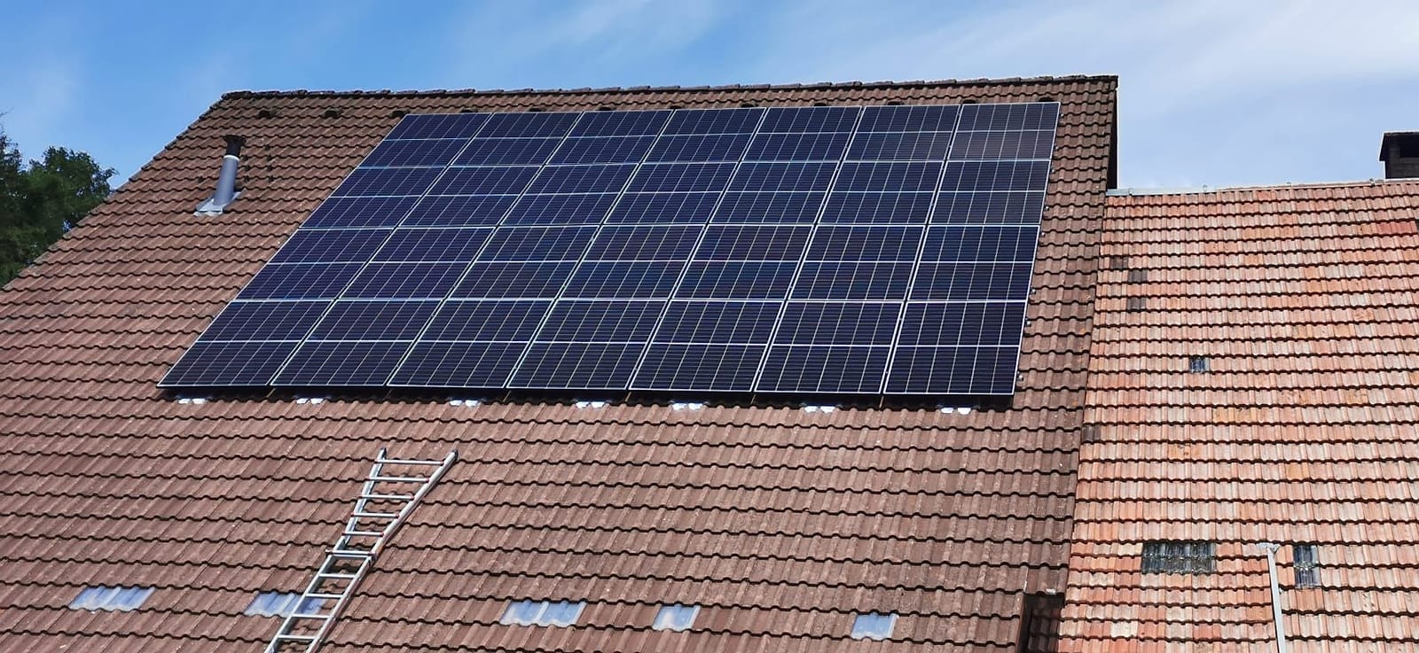 Fertig montierte Photovoltaikanlage mit 28 Modulen auf einem roten Ziegeldach vor blauem Himmel