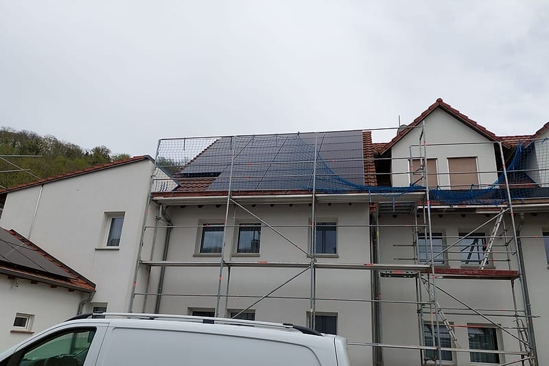 Mehrfamilienhaus im Baugerüst mit fertig montierter Photovoltaikanlage auf dem Dach