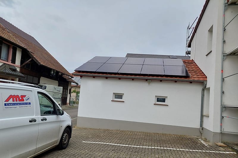 Zehn schwarze Photovoltaikmodule auf dem Dach eines Nebengebäudes, davor das Servicefahrzeug der MS Elektrotechnik