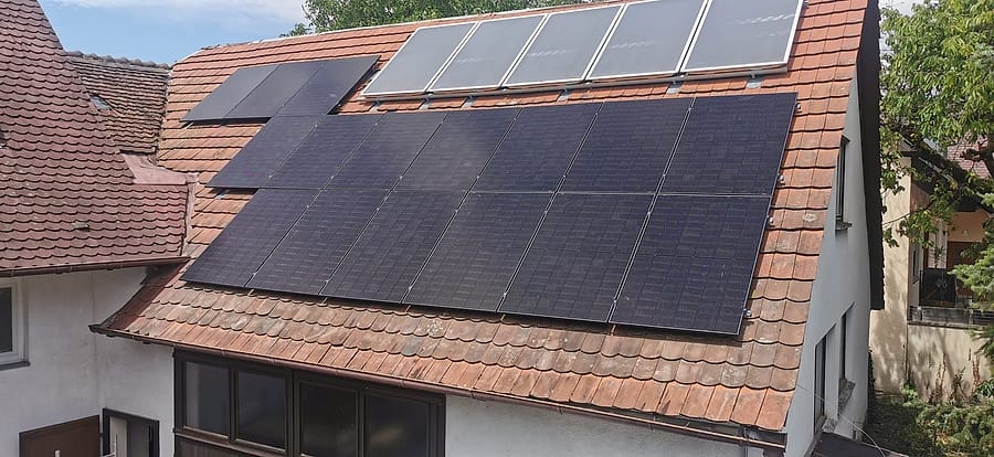 Ziegeldach mit schwarzen Photovoltaikmodulen unterhalb bereits vorhandener Solarthermie-Kollektoren